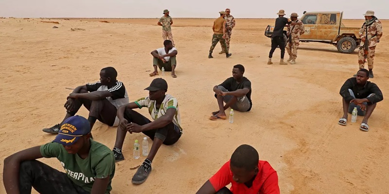 des migrants dans le désert du Sahara sous la surveillance de policiers d'Etat